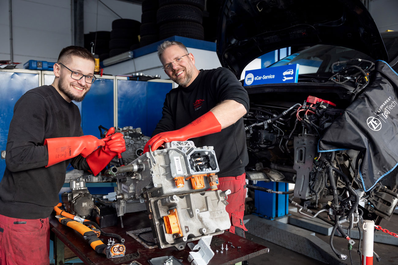 Foto: zwei Kfz Mechaniker stehen hinter einem Elektromotor