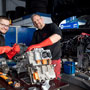 Foto: zwei Kfz Mechaniker stehen hinter einem Elektromotor